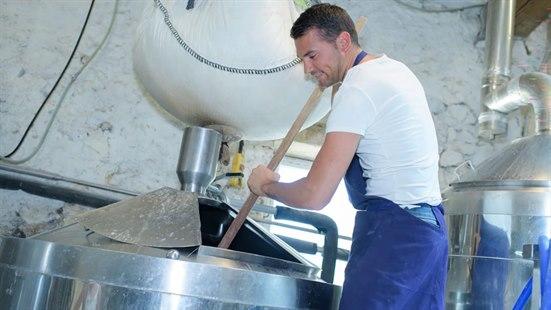 Fotoet viser en mann som står ved en stor gryte i et industrielt bakeri og rører deig. 