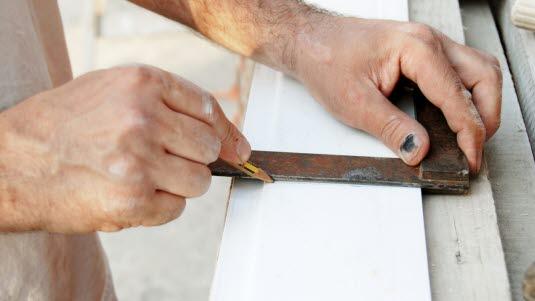 Håndverker med blå negl som lager kappemerke på en planke