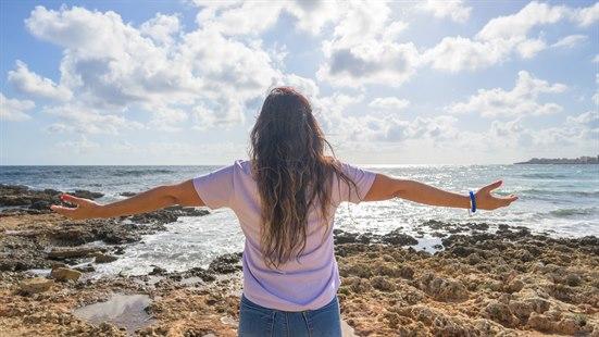 Illustrasjonsfoto av en kvinne som ser utover havet og strekker armene ut til siden.