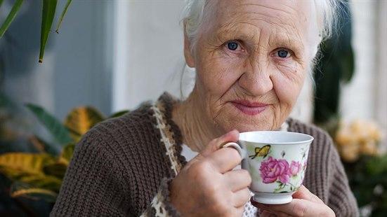 Nærbilde av en eldre dame som holder en kaffekopp i porselen