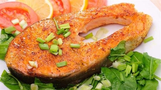 Middagstallerken med en laksefilet og oppkuttet grønnsaker som tomat, sitron, spinat og purreløk