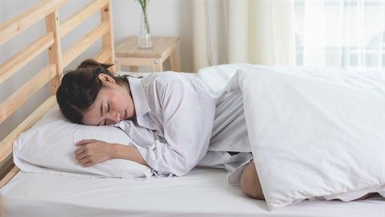 Kvinne i hvitt nattøy sover i en enkeltseng