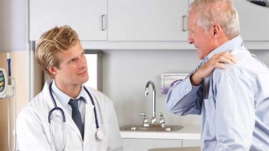 Bildet viser mannlig lege som undersøker mannlig, eldre pasient som holder seg til venstre skulder med høyre arm, og angir smerter i venstre skulder. 