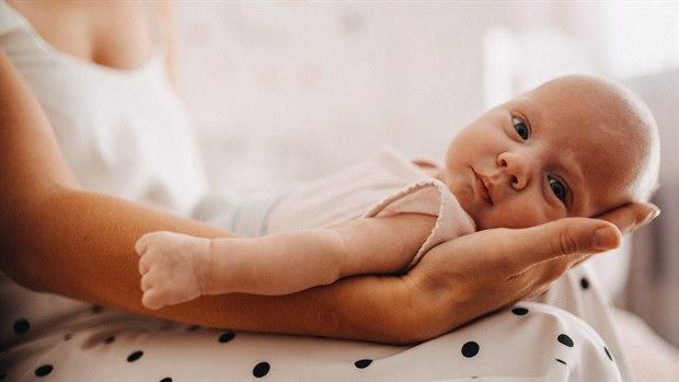 Illustrasjonsfotoet viser en baby som ligger i fanget på moren sin. Babyen ser rett i kameraet.