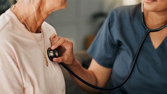Illustrasjonsfotoet viser en sykepleier som holder et stetoskop mot brystet til en eldre kvinnelig pasient. De sitter i en stue på et eldrehjem.