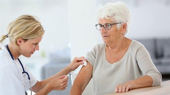 Ung kvinnelig helsearbeider i hvilt kittel setter vaksine på eldre kvinne