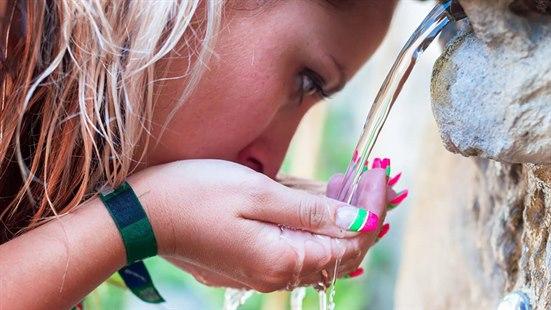 En kvinne holder hendene under en rennende vannfontene for å drikke. Mens vannet renner ned i hendene hennes og hun tar en slurk.