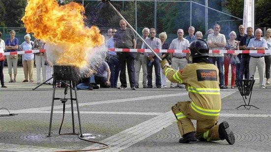 Illustrasjonsfoto: En brannmann demonstrerer hva som skjer når det tar fyr i en kjele med olje. En gruppe mennesker står bak et sperrebånd og ser på.