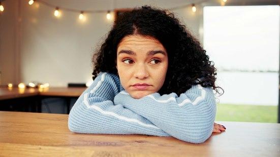 Illustrasjonsfoto: Ung kvinne hviler armene på en kjøkkenbenk og haken på armene.