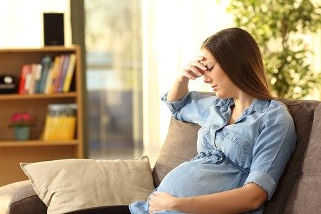 Bekymret gravid kvinne som sitter på en sofa i stuen