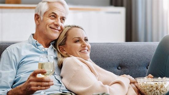 Illustrasjonsfoto av et middelaldrende par som ser på tv, spiser popcorn og drikker vin.