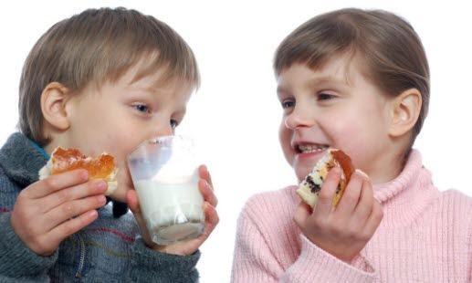 To småbarn som sitter og spiser sjokoladeboller med et glass melk 