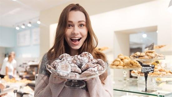 Ung dame holder et kakefat med småkaker foran seg. Bakeridisk i bakgrunnen.