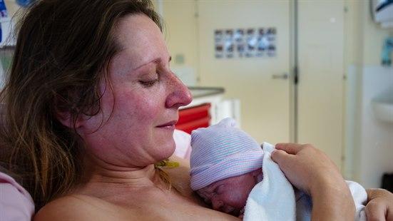 Illustrasjonsfoto viser en mor som holder sitt nyfødte barn tett inntil brystet, liggende i en sykehusseng
