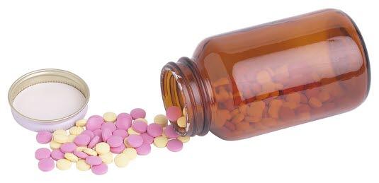 Pilleglass med piller i og utenfor glasset