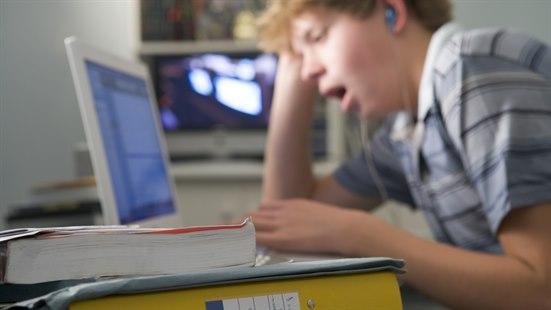 Illustrasjonsfoto av ung gutt som gjør skolearbeid foran en pc-skjerm og gjesper.