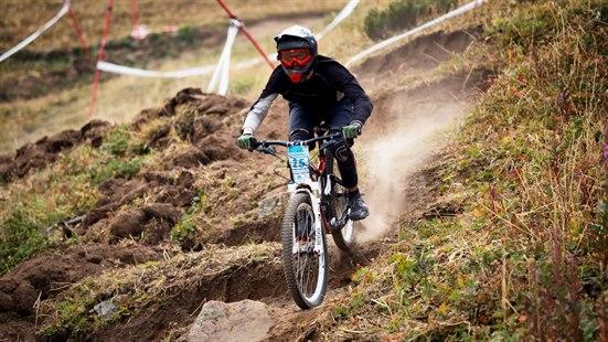 Illustrasjonsfoto: Terrengsyklist som sykler ned en bratt, humpete bakke. Syklisten er kledt i mørke klær og bruker hjelm og beskyttelsesbriller.