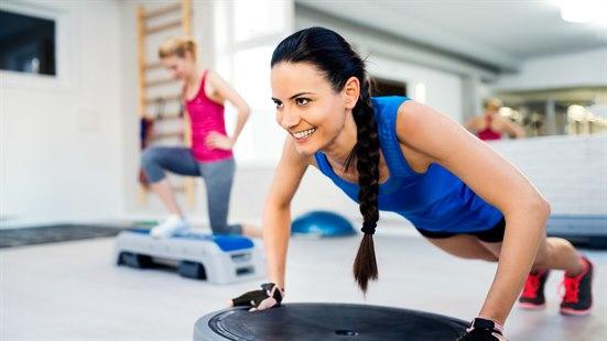 Illustrasjonsfoto: Ung dame med langt mørkt hår trener armhevinger på bosuball i et treningssenter.