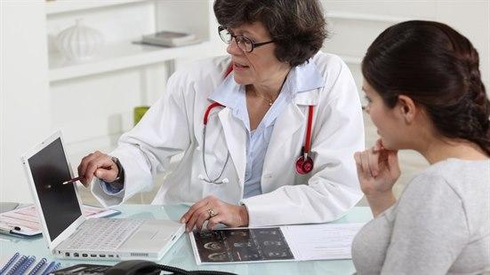 Illustrasjonsfotoet viser gravid kvinne og en kvinnelig lege. Legen peker på datamaskinens skjerm