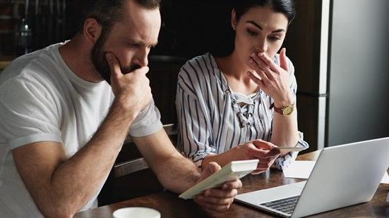 Illustrasjonsfoto av et ungt, bekymret par som sitter foren en pc og med en kalkulator.