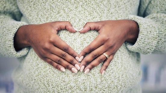 Illustrasjonsfoto av en gravid kvinne som former et hjerte med hendene over magen. Vi ser et nærbilde av magen.