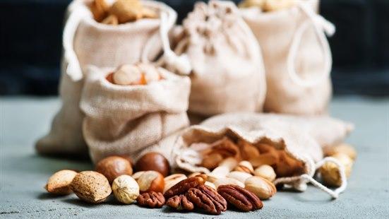 Illustrasjonsfoto av små tøyposer fylt med nøtter. En pose ligger vendt mot oss med forskjellige nøttetyper spredt foran den.