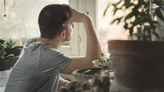 Ung mann ser ut av vinduet, han støtter hodet i den ene hånda.