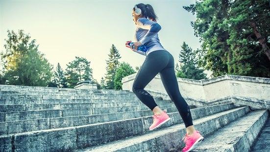 Ung kvinne i treningsklær og rosa joggesko løper i en stor, utendørs steintrapp.