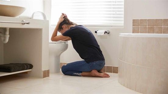 Illustrasjonsfoto: Kvinne sitter på badegulvet foran do, lener seg mot toalettskålen.