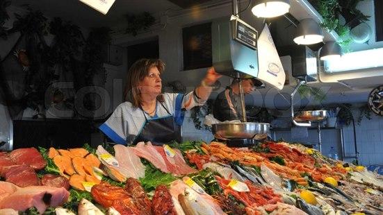Fotoet viser en dame som veier fisk i en sjømatsbutikk. Litt til høyre står en yngre mann og jobber med varene. 
