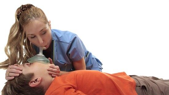 Illustrasjonsfoto av en dame som utfører munn-til-munn metode på en ung gutt. Hun bruker en oksygenmaske til å gjennomføre innblåsingene.