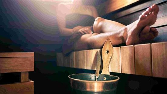 Kvinne sitter med beina strekt foran seg i en badstu. Bøtte med vannøse i forkant.