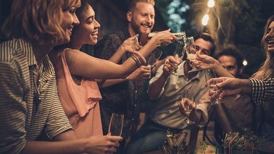 Illustrasjonsfoto av en gruppe pent kledde mennesker som skåler og smiler på en utendørsfest i en hage.