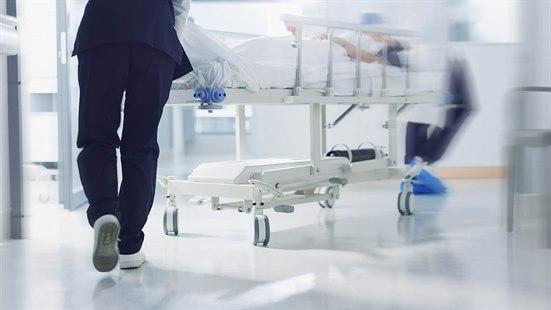 Illustrasjonsfoto av to helsepersonell som løper i en sykehuskorridor med en pasient i en sykeseng.