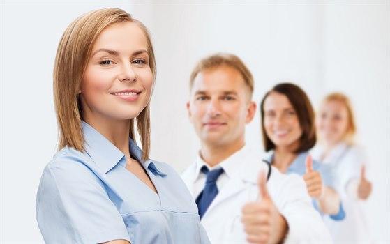 4 helsepersonell, ung kvinne framst. De andre litt uskarpe i bakgrunnen. Alle viser tommel opp til hun i front.