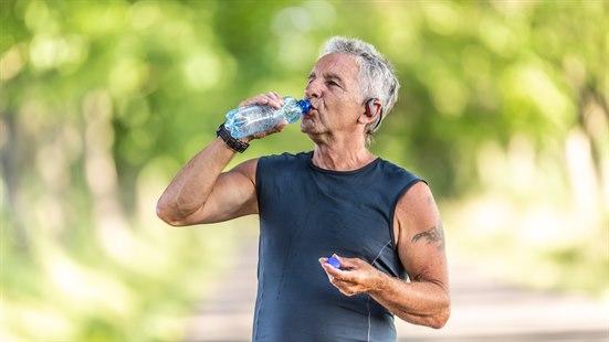 Illustrasjonfoto av en eldre mann som trener i varmen og som drikker vann fra ei flaske.
