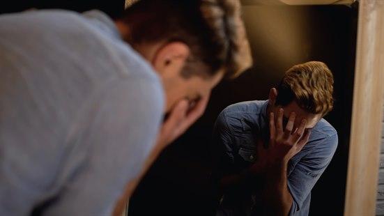 Illustrasjonsfoto av fortvilet ung mann som skjuler ansiktet sitt med hendene.