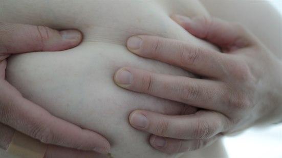 Nærbilde av et bryst fra siden, kvinnen har begge hender på brystet og undersøker det