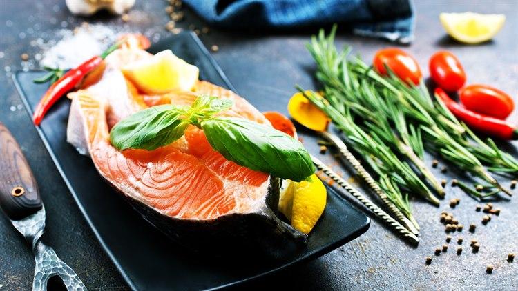 Illustrasjonsfoto av en laksefilet på et fat, omgitt av en fargerik blanding av grønnsaker som basilikum, sitron, chilli og krydder urter.