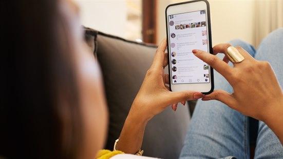 Illustrasjonsfoto av en kvinne som ligge rpå sofaen og scroller på en smarttelefon.