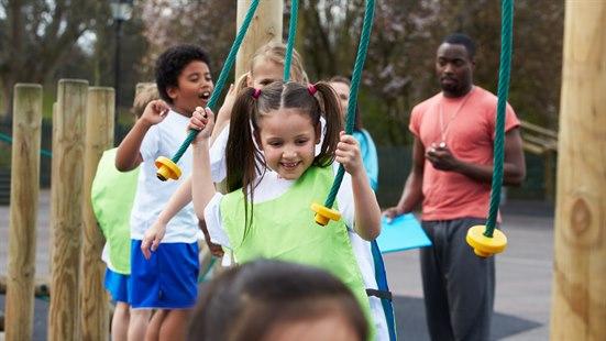 En gruppe barn som har gym, balanserer. Gymlærer i bakgrunnen med stoppeklokke.