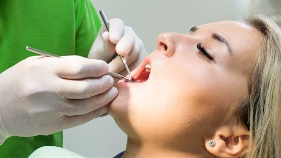 Tannlege undersøker tennene til kvinnelig pasient.