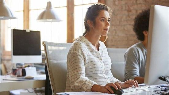 Illustrasjonsfoto av gravid kvinne som sitter på arbeidsplassen og ser inn mot skjermen. Hun ser fokusert ut.