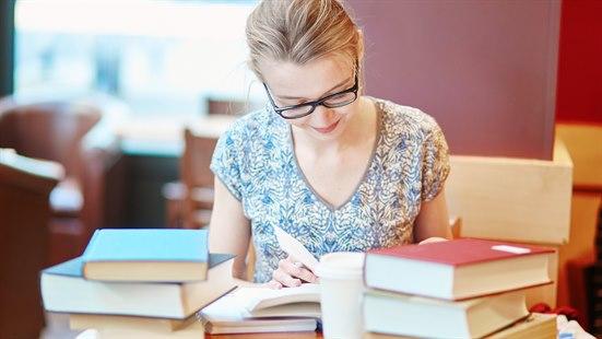 Illustrasjonsfoto av en kvinne som sitter og studerer til eksamen. Det er flere bøker stablet oppover hverandre på bordet foran henne.
