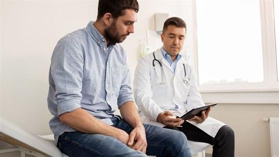 Illustrasjonsfoto viser en mann som sitter ved siden en lege i hvit frakk med steoskop rundt halsen. Legen viser noe på et nettbrett.