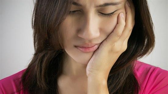 Illustrasjonsfoto av ung kvinne som holder en hånd over kjeven og ser plaget ut