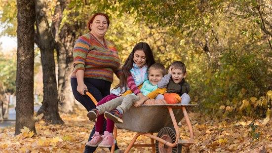 Illustrasjonsfoto av en kvinne som har det morsomt sammen med tre barn. Det er høst og barna trilles i en trillebår.