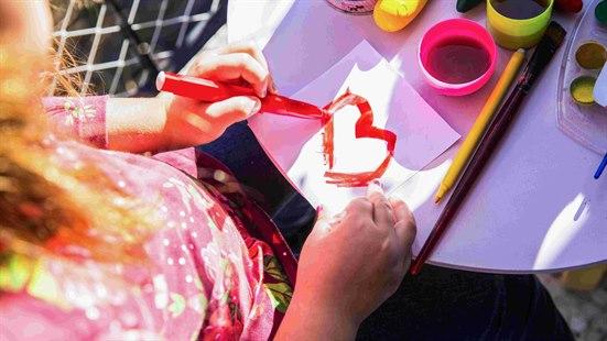Illustrasjonsfoto: Barn som maler et hjerte. Malesaker står på bordet ved arket hen maler på.