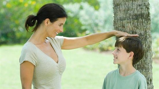 Illustrasjonsfotoet viser en kvinne og en gutt. Gutten står inntil et tre og kvinnen måler høyden hans med hånden