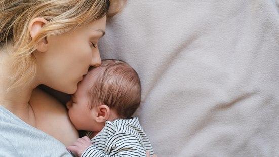 Illustrasjonsfotoet viser nærbilde av en nybakt mor og hennes barn. De ligger på siden med ansiktet vendt mot hverandre